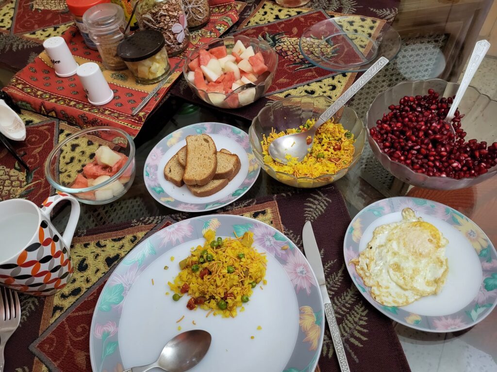 An appetizing breakfast spread with sunny-side-up fried eggs, fragrant poha, fresh fruits, and crisp toast.